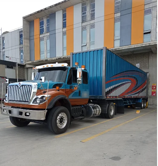 Tractomula International azul y naranja con contenedor frente a una bodega
